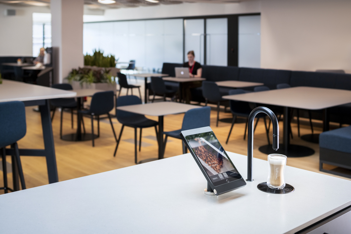 Matte black TopBrewer with deluxe iPad holder in the foreground and person working on laptop in background